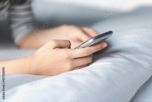 Woman hand using mobile phone on bed.