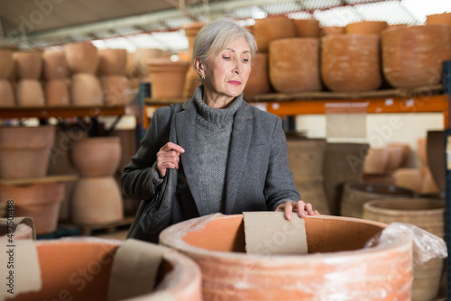 Gray haired woman selecting decorative earthenware pot in home goods store.