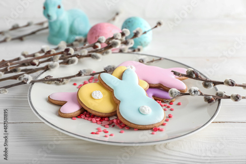 Plate with tasty Easter cookies in shape on bunny and pussy willow branches on white wooden background