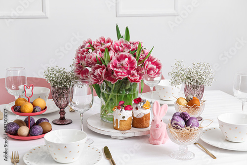 Beautiful tulips, Easter cakes, eggs and dinnerware on served table © Pixel-Shot