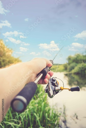 Male hand holds spinning rod on the background of the river.