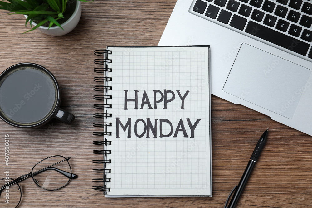 Message Happy Monday written in notebook, laptop and cup of coffee on wooden desk, flat lay