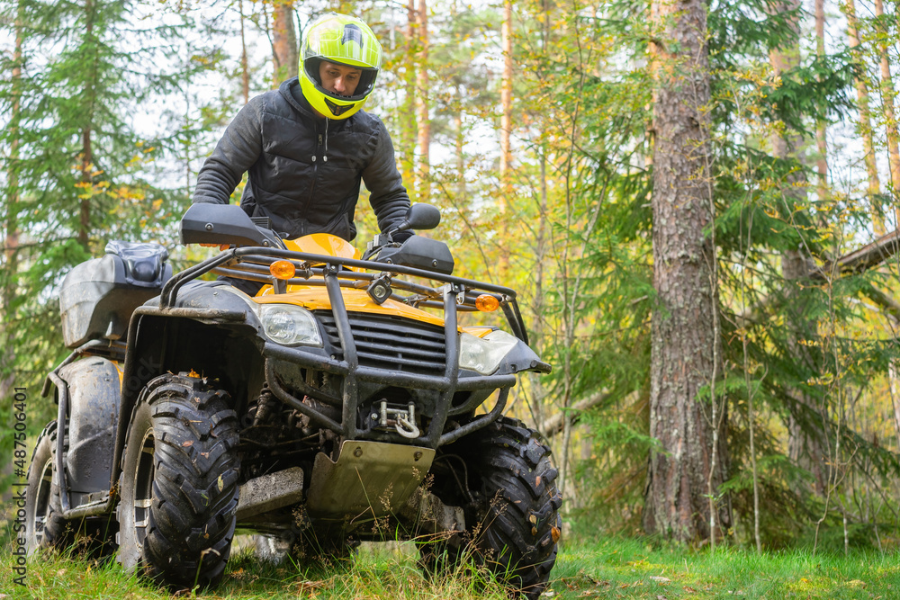 Fototapeta premium ATV rider during motocross. ATV rider in taiga. Man on yellow quadcycle. Participates in off-road race. Extreme man. Motocross in forest. Extreme sport on bike. ATV rides through green forest.