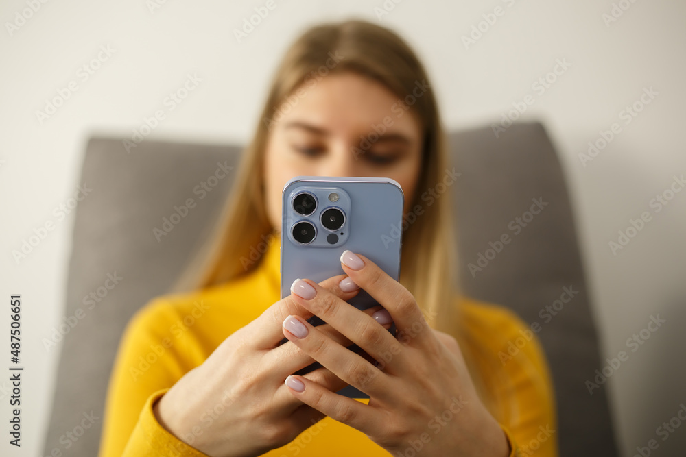 Using mobile phone for communication. Young blonde woman typing message in mobile messener app while sitting on couch in apartment. Beautiful white female texting online in social media application Using mobile phone for communication. Young blonde woman typing message in mobile messener app while sitting on couch in apartment. Beautiful white female texting online in social media application