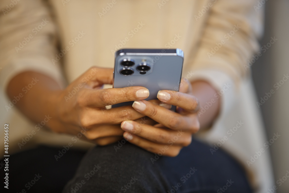 Young black woman texting in messenger app on smartphone. African female using modern blue mobile phone for communication online. Person holding new cellphone with triple camera Young black woman texting in messenger app on smartphone. African female using modern blue mobile phone for communication online. Person holding new cellphone with triple camera