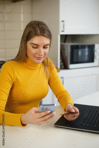 Beautiful white blonde woman paying with credit card in mobile app. Cheerful customer making puchase in internet store with bank card. Happy young female making money transfer in modern smartphone