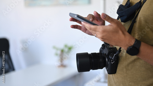 Young male photographer standing in modern studio and using smart phone.