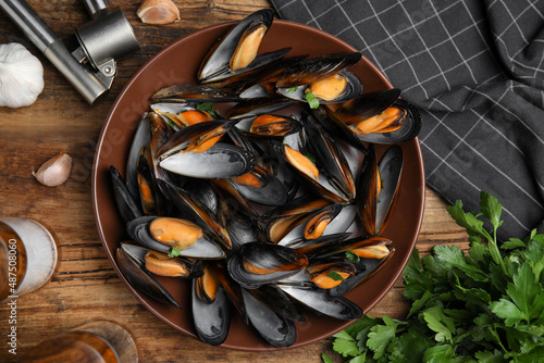Plate of cooked mussels with parsley and garlic on wooden table, flat lay
