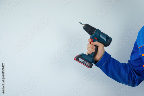 A male repairman in work clothes holds a screwdriver in his hand in a room with a white wall.