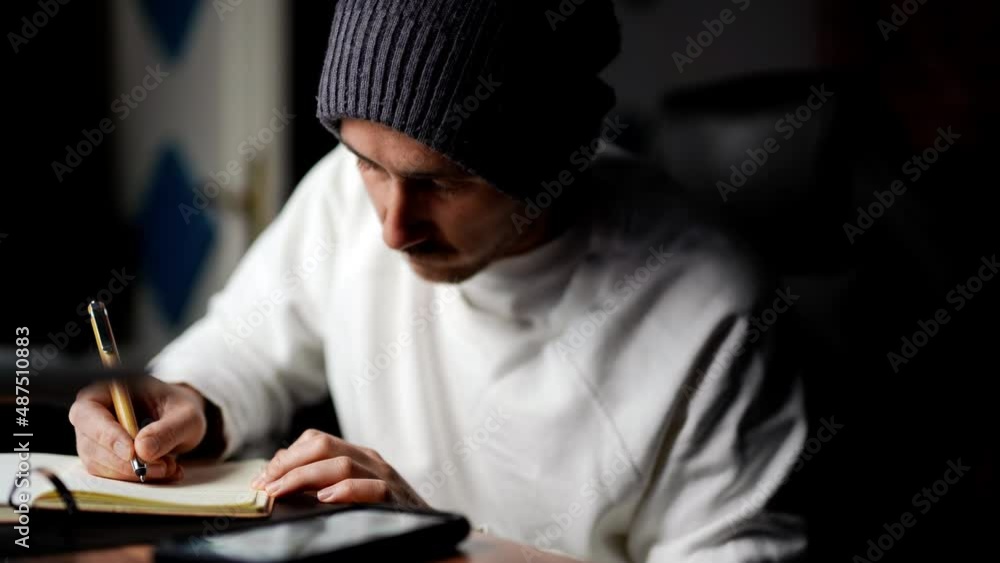 Modern Caucasian young male writing on paper notebook new ideas get distracted from a message on his modern smartphone device Modern Caucasian young male writing on paper notebook new ideas get distracted from a message on his modern smartphone device