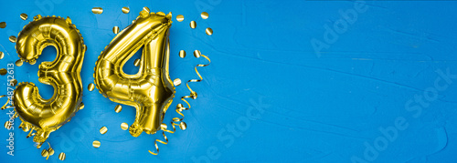 golden foil balloon number thirty four. Birthday or anniversary card with the inscription 34. blue concrete background. Anniversary celebration. Banner. photo