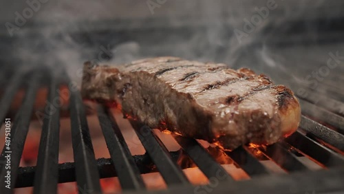 Roasting juicy meat steak with spices and herbs in burning charcoals fire on bbq grid, flames and smoke. Barbecue grill