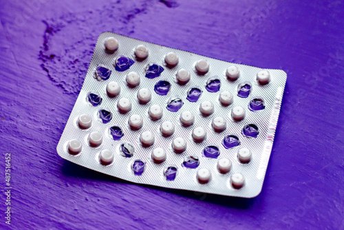 in a blister with white tablets, empty squeezed cells form the shape of a heart on a purple uneven surface photo