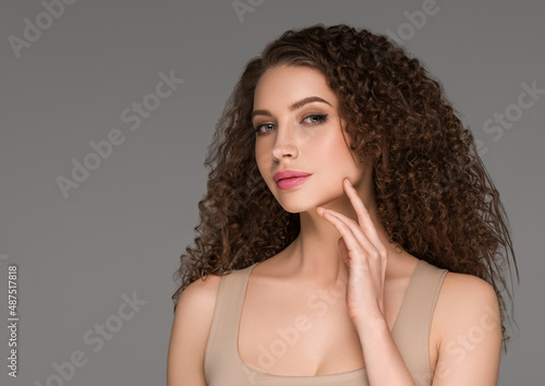 Curly long brunette hair woman touching face beauty close up female portrait. Color backgound gray