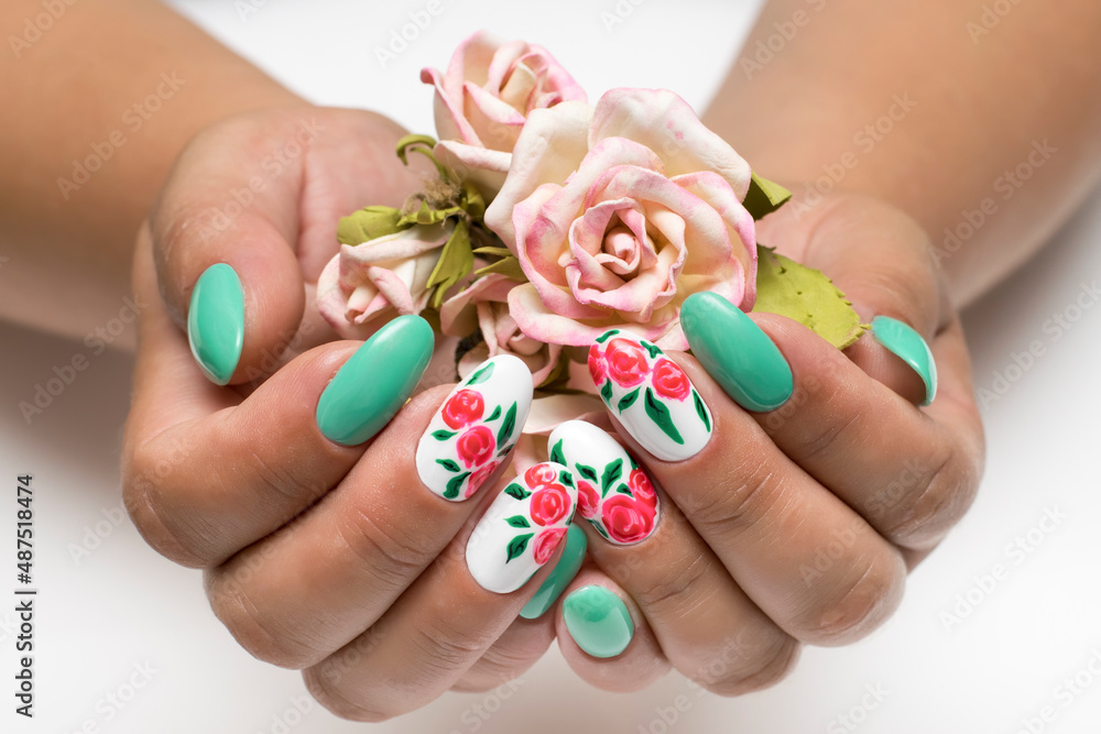 Mint white manicure on long oval nails with painted red flowers on a white background close-up with roses in the palm.