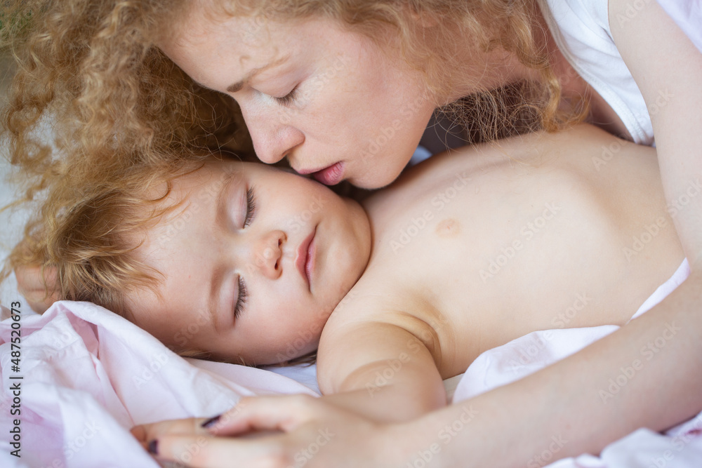 Mother and baby sleeping in the bed. Mother kiss sleepy child. Childhood and family concept, close-up indoor portrait. Mother and baby sleeping in the bed. Mother kiss sleepy child. Childhood and family concept, close-up indoor portrait.