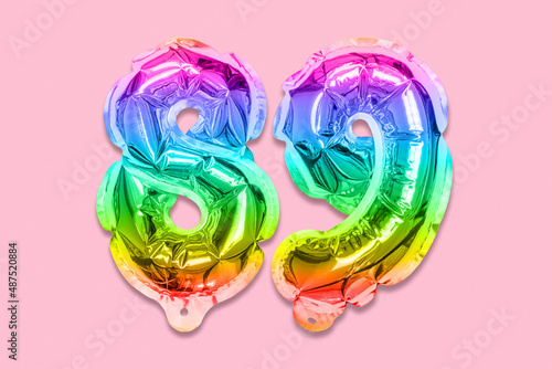 Rainbow foil balloon number, digit eighty nine on a pink background. Birthday greeting card with inscription 89. Top view. Numerical digit. Celebration event, template. photo