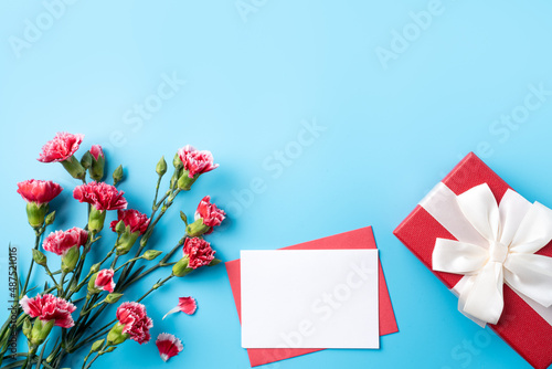 Mother's Day gift. Design concept of holiday greeting card with red carnation bouquet on bright blue table background