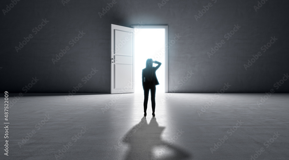 Obraz premium Successful business woman standing in front of bright success door in concrete interior with shadow on floor. Future and dream concept.