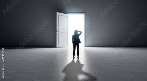 Successful business woman standing in front of bright success door in concrete interior with shadow on floor. Future and dream concept.