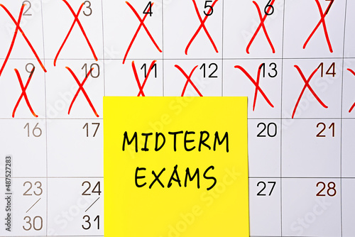 The phrase Midterm exams written on a yellow sticky note posted on a calendar or planner page as a reminder. Closeup of a personal agenda