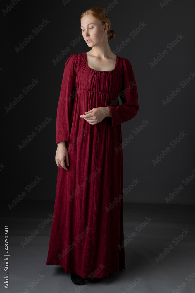 A Regency woman wearing a simple red linen day dress against a studio back drop A Regency woman wearing a simple red linen day dress against a studio back drop