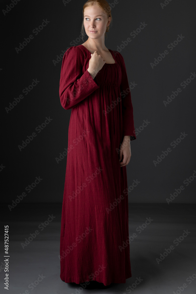 A Regency woman wearing a simple red linen day dress against a studio back drop