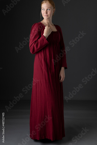 A Regency woman wearing a simple red linen day dress against a studio back drop