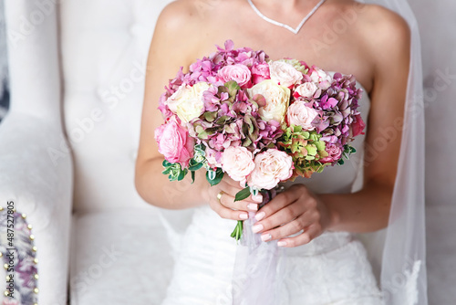 the bride in a white slinky dress holds a wedding bouquet of pink peonies