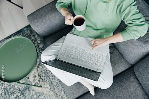 Woman working at home using laptop and drinking coffee, top view close-up