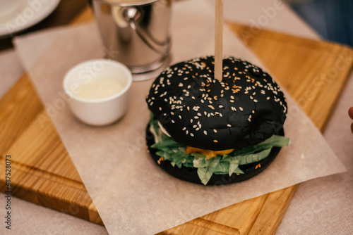 Canvas Print Big tasty delicious black sesame benne ham burger with stick, green, lettuce near garlicky white sauce in pannikin plate gravy boat