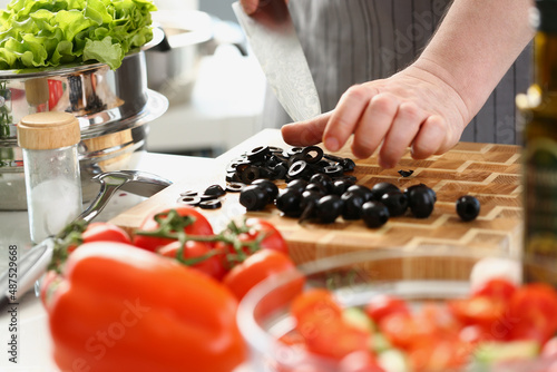 Fototapeta Naklejka Na Ścianę i Meble -  Man chef cutting olives on wooden cutting board, add ripe vegetable to salad