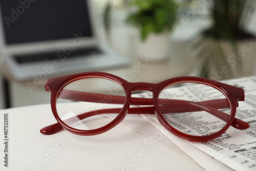 Glasses and newspaper on armrest indoors, closeup