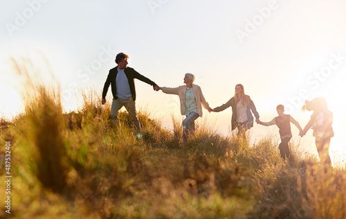 Grandpa is in the lead. Shot of a multi-generational family walking hand in hand across a field at sunset. photo