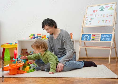 Father and sweet little child boy having fun playing with cars and colorful toys, on the floor, at home. Beautiful family moment, indoors