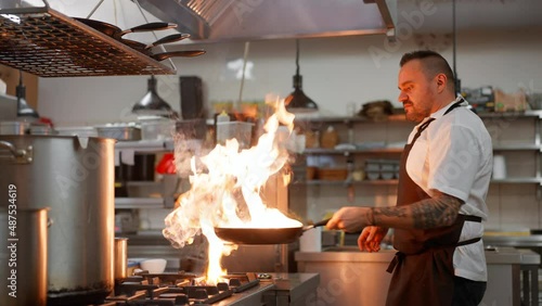 Professional chef preparing meal, flambing indoors in restaurant kitchen. photo