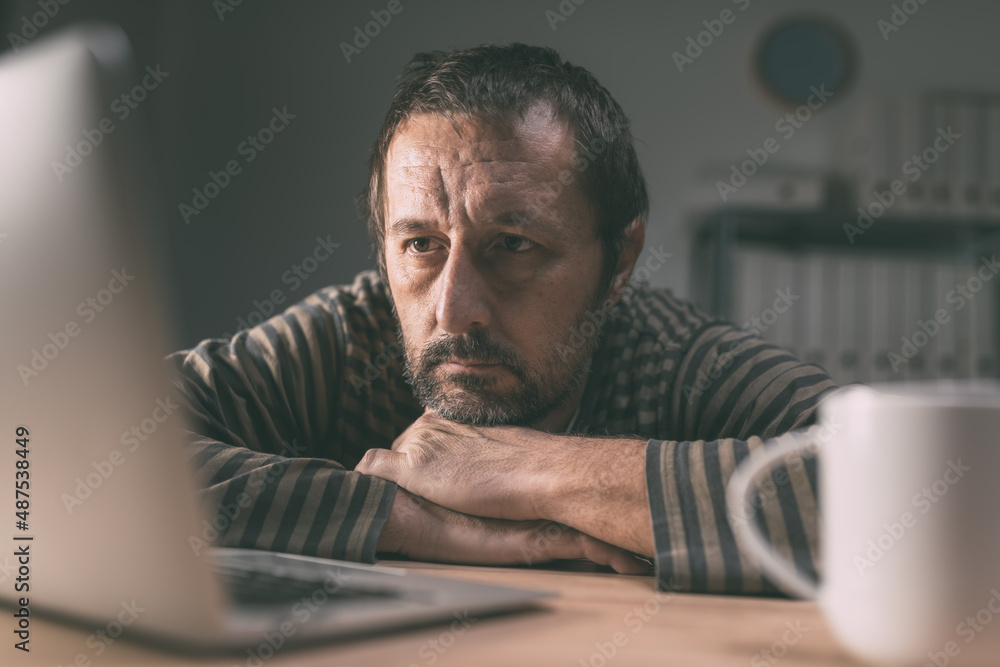 Lethargic employee looking at laptop computer screen in business office late at night Lethargic employee looking at laptop computer screen in business office late at night