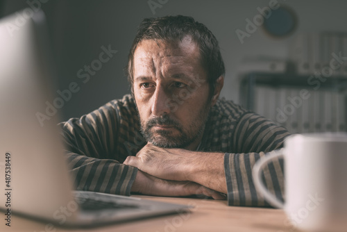 Lethargic employee looking at laptop computer screen in business office late at night photo