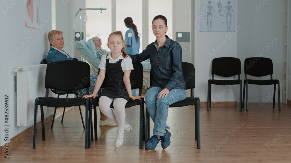 Portrait of mother and little girl in waiting room at clinic. Woman with child sitting in reception lobby, waiting to go to medical appointment and annual checkup visit with physician. Portrait of mother and little girl in waiting room at clinic. Woman with child sitting in reception lobby, waiting to go to medical appointment and annual checkup visit with physician.