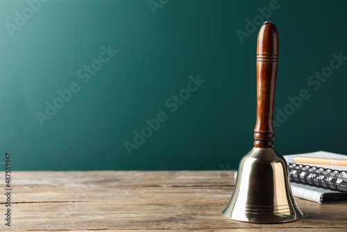 Golden bell and notebooks on wooden table near green chalkboard, space for text. School days