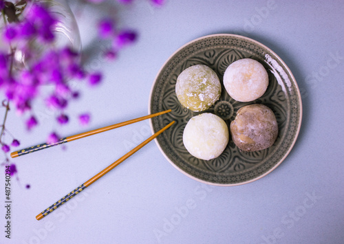 Traditional Japanese dessert mochi in rice dough or daifuku. Mochi ice cream balls on gray plate, food chopsticks on violet blue background top view. Table setting and flowers decor. Selective focus.