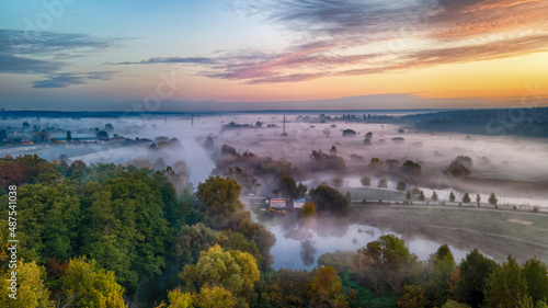 Foggy field with forest before dawn from a bird's-eye view. Clear and gloomy pink-purple sky.