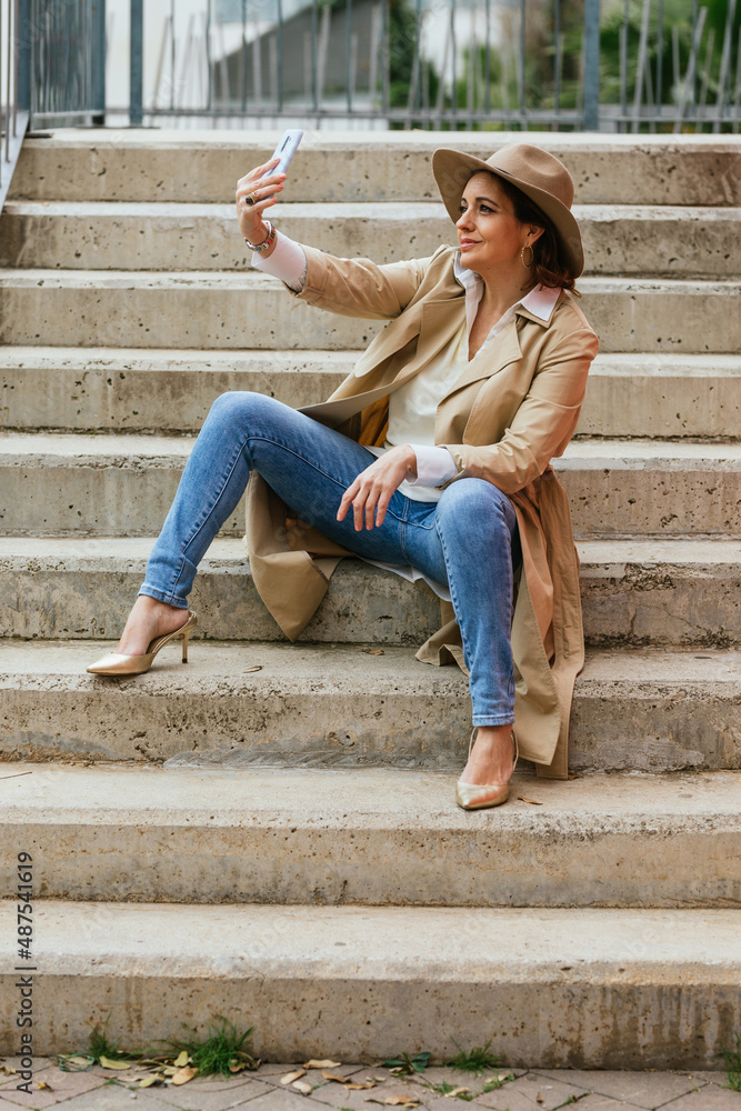 An elegant adult woman sitting on steps outdoors and taking a selfie An elegant adult woman sitting on steps outdoors and taking a selfie