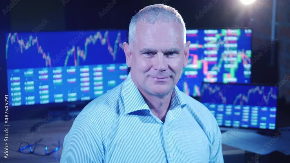 Male broker next to the monitors showing stock market data