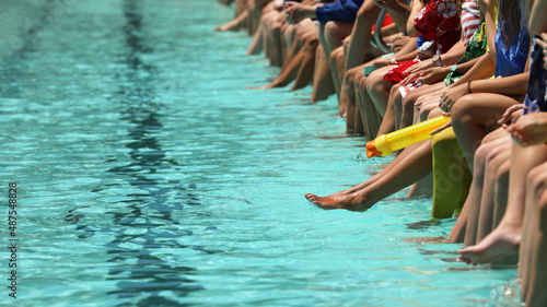 Vászonkép A bright aqua blue swimming pool with students sitting dangling their feet and toes in the water spectating