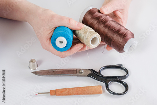 Woman holds spools of thread of different colors in her hands. There are scissors and a seam ripper on the table. Seamstress workplace, tools for sewing and repair clothes.