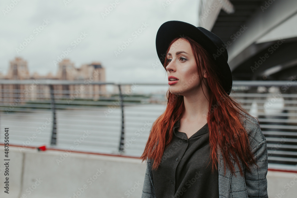 young woman with red hair outdoors in a coat and hat