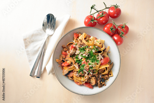 Tagliatelle with sauce from minced meat, tomatoes and vegetables with parmesan and parsley garnish on a plate and a light wooden table, copy space, high angle view from above, selected focus