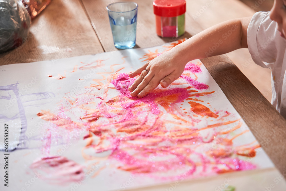 Cute child drawing with hand at the paper and putting glitter at her picture Cute child drawing with hand at the paper and putting glitter at her picture