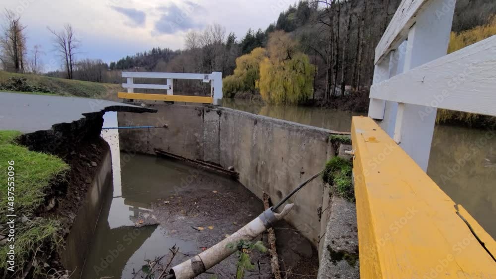 The camera pans over a water canal where the road collapsed during a storm The camera pans over a water canal where the road collapsed during a storm